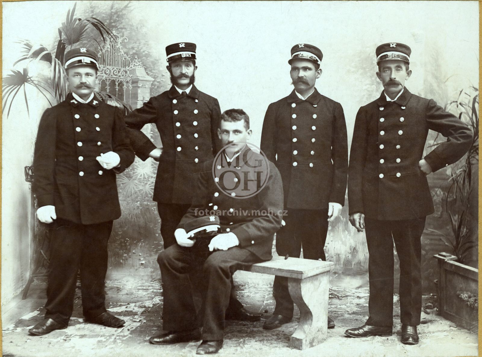 Fotografie - Poštovní zřízenci. Poštovní  zaměstnanci, sluhové (zřízenci) patrně ve stejnokrojích vzor 1902. Odznak tvaru poštovního rohu umístěný na čepici označoval poštovního sluhu v netechnických službách, tzn. poštovním provozu v užším smyslu. Telegr